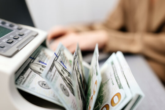 Close-up of hands counting US dollar bills in an automatic cash counter. Ideal for financial, banking, and currency exchange themes. Perfect for promoting financial services and business solutions.
