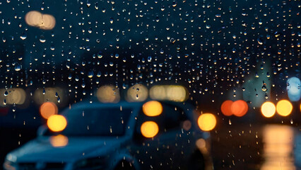 Raindrops on a car window with blurred city lights in the background, creating a moody atmosphere