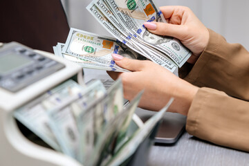 A businesswoman uses a money counter at her desk, with focus on financial management and precision in business operations. Ideal for themes of finance, accounting, and successful entrepreneurship.