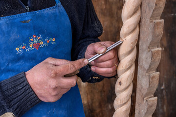 craftsman in an embroidered blue apron works a twisted wooden column using a gouge