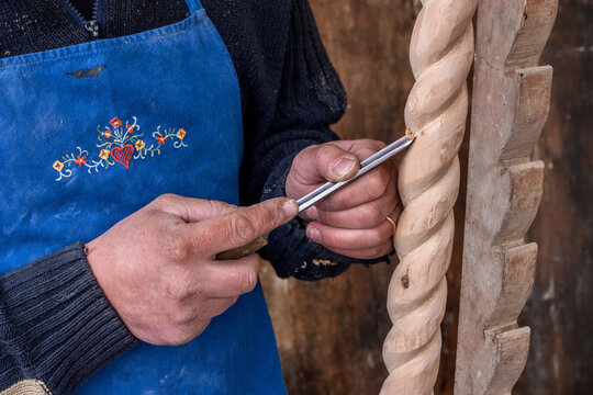 craftsman in an embroidered blue apron works a twisted wooden column using a gouge