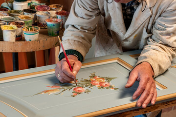 craftsman decorates with brush and colors the door of a wardrobe in typical style
