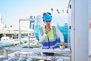 Technician talking on walkie talkie and checking pipeline valves or water tank area at urban...