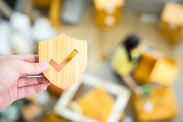 A moving company employee holds a insurance symbol with blurred image of a woman lifting things to move into a house. The concept of insurance for damages when moving into a new home.