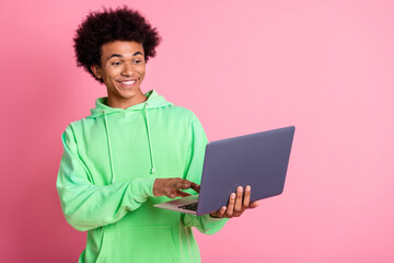 Portrait of cool young man use laptop empty space wear green hoodie isolated on pink color...