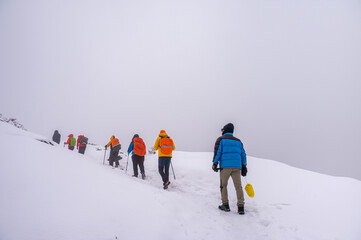 Group of hikers trekking through a snowy mountain trail in foggy conditions, wearing colorful winter gear. Adventurous winter expedition in a remote, cold landscape.

