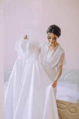 A woman is holding a white dress in front of a mirror. Concept of elegance and sophistication, as the woman prepares for a special occasion