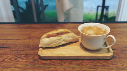 Morning hot Coffee with Cappuccino and vietnamese bread served on Wooden Tray,  placed on rustic wooden table by Window with natural view. Food and drink concept.