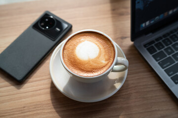Close-up of Hot coffee latte with latte art milk foam in cup mug and laptop computer and smartphone on wood desk office desk in coffee shop at the cafe,during business work concept