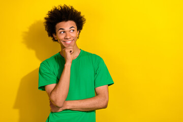 Photo of attractive funny guy wear green t-shirt arms chin looking emtpy space isolated yellow...