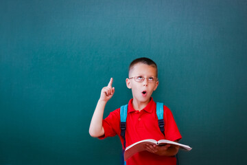 A Happy child child standing at the blackboard with a school backpack wearing glasses