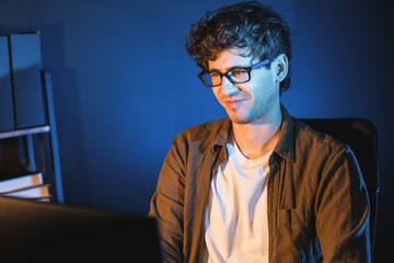 Smiling young businessman focusing on pc for creative startup project job at neon light modern office. Thinking marketing network online planning of creator to market channel design concept. Gusher.