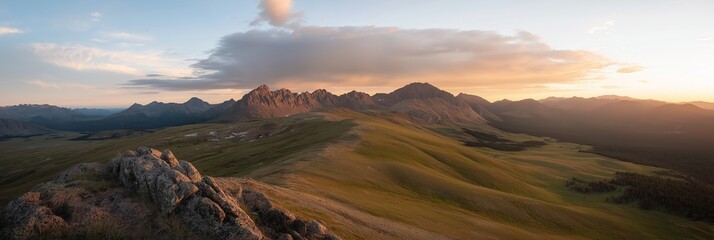 Panoramic view of a mountain range at sunrise, showcasing vast green valleys and scattered clouds in the sky.