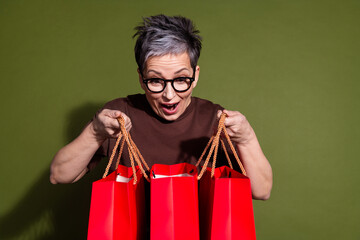 Photo of nice aged woman look shop bags wear brown t-shirt isolated on khaki color background