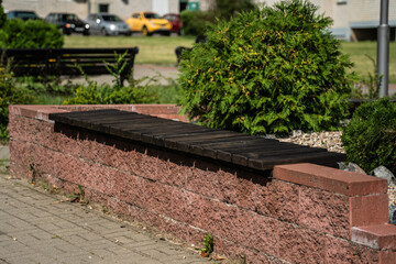 An outdoor, wooden bench without a back is mounted on a high curb