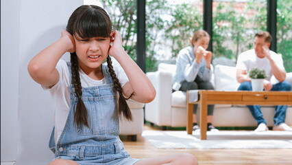 Stressed and unhappy young girl huddle in corner, cover her ears blocking sound of her parent arguing in background. Domestic violence at home and traumatic childhood develop to depression. Synchronos