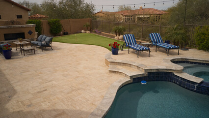 An aerial view of a desert landscaped backyard featuring a travertine pool deck with an outdoor kitchen, fireplace, pool and spa.