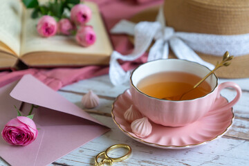A cup of aromatic tea, a book and a rose on the table.