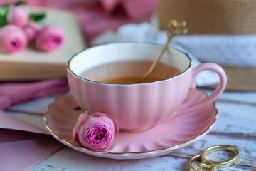A cup of aromatic tea, a book and a rose on the table.
