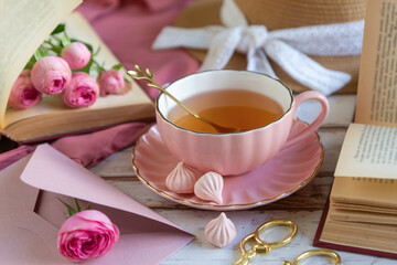 A cup of aromatic tea, a book and a rose on the table.