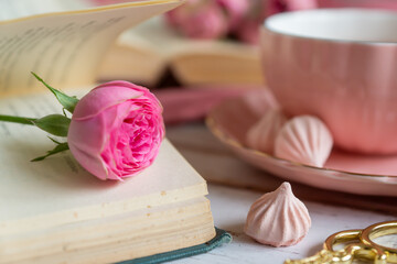 A cup of aromatic tea, a book and a rose on the table.