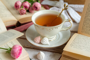 A cup of aromatic tea, a book and a rose on the table.