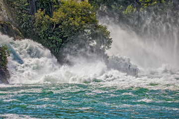 a little man stands between the roaring rhine waterfall with high waves and lots of spray
