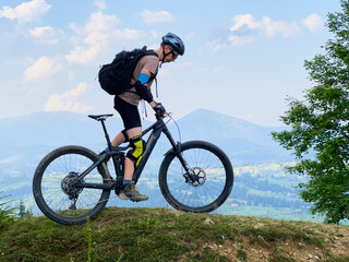 Cyclist man riding electric mountain bike outdoors. Male tourist biking along grassy trail in the...