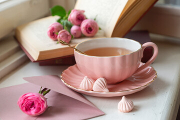 A cup of aromatic tea, a book and a rose on the table.