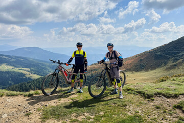 Two cyclists men riding electric bikes outdoors. Portrait of male tourists resting on the top of...