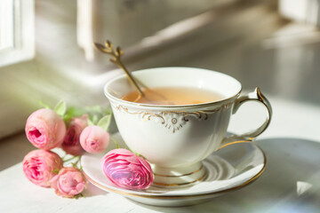 A cup of aromatic tea, a book and a rose on the table.