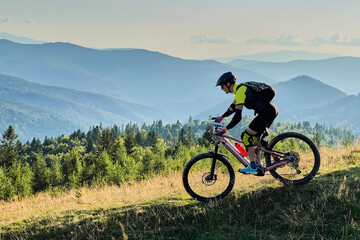 Fototapeta premium Cyclist man riding electric mountain bike outdoors. Male tourist biking along grassy trail in the mountains, wearing helmet and backpack. Concept of sport, active leisure and nature.