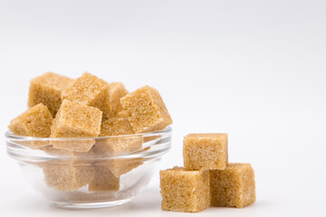 Brown cane sugar cubes in a glass bowl on white background with copy space