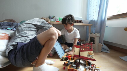 Two boys engrossed in playing with toy figures and vehicles, searching in plastic bucket on bedroom...