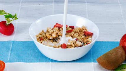 Close up of a white bowl of cereal with milk being poured into it. Macrography of white milk pouring in to bowl with cornflake, dry fruit and splashing milk with isolated white background. Pabulum.