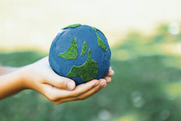 Young boy's hand holding planet Earth globe at natural park background as Earth day to save this planet with ESG principle and environment friendly energy for brighter future. Gyre