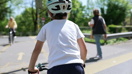 Young boy with helmet on bike, back view, crossing street, sunny day, child safety, outdoor...