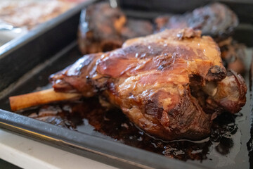 A close-up of a perfectly roasted lamb shank, resting in its juices in a baking tray