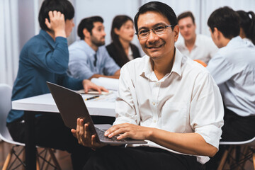 Confidence and happy smiling businessman portrait with background of his colleague and business team working in office. Office worker teamwork and positive workplace concept. Prudent