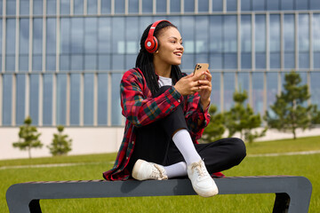 Amidst the beauty of the outdoors, a woman of African-American descent indulges in her preferred musical realm via her phone.