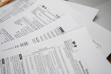 Tabletop cluttered with diverse tax forms signifying annual tax preparation ritual capturing...