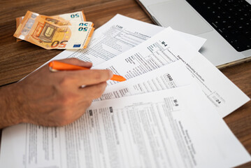 Obraz premium Man entrepreneur engages in paperwork filling complicated tax forms mandatory for business owners sitting at workplace with euro banknotes and laptop in office