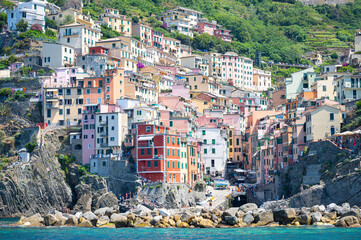 Riomaggiore, Italy - July 18, 2024: Picturesque view from the sea of colored houses on a steep cliff in the historic town of Riomaggiore, part of Cinque Terre on the Ligurian coast, Italy.