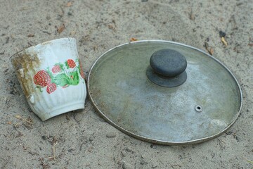 one empty coffee ceramic discarded old white dirty beautiful broken without handle industrial with strawberry pattern cup with glass lid from frying pan lie on the ground during daytime outdoors
