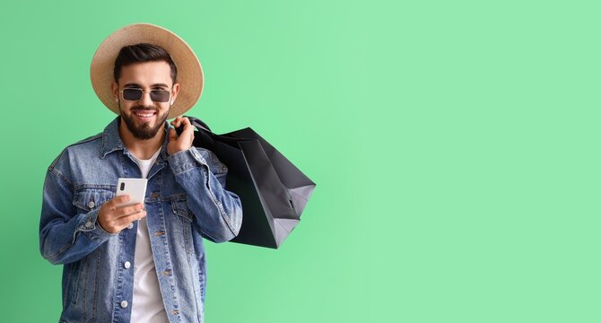 Handsome man with mobile phone and shopping bags on green background with space for text - Powered by Adobe