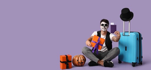 Male tourist dressed for Halloween, gift, pumpkin and suitcase on lilac background with space for...