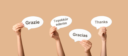 Hands holding speech bubbles with text THANK YOU in different languages on beige background © Pixel-Shot