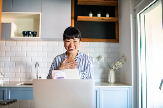 Happy Asian woman opening package in the kitchen