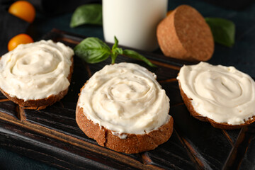 Wooden board of tasty sandwiches with cream cheese on black background