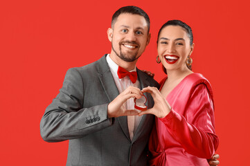 Happy engaged couple making heart with their hands on red background